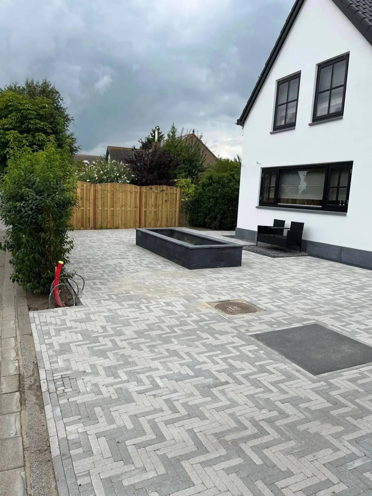 Visgraatbestrating met verhoogde plantenbak en grindstrook langs de gevel