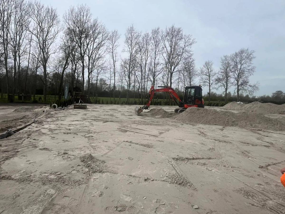 Minigraver egaliseert een groot zandbed op een buitenterrein